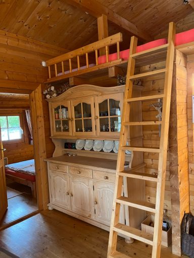 Wohnraum Holzhütte mit einer Treppe zum Schlafbereich und einem Schrank mit Geschirr.