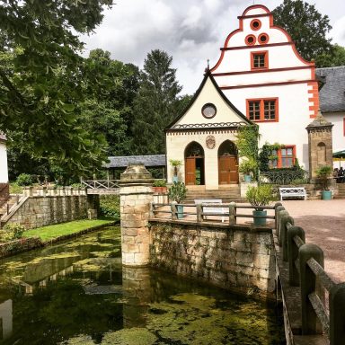 Schloss Kochberg Historisches Gebäude mit roten Akzenten, umgeben von Grün und einem Teich.