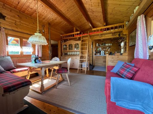 Wohnraum Gemütliches Holzhaus mit Sitzbereich, Esstisch und offener Küche. Helle Fenster und warme Farben.